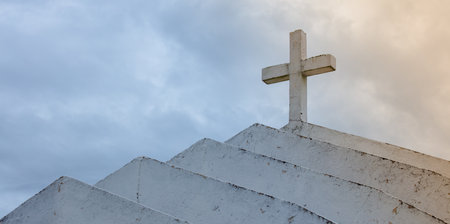 A closeup shot of a roof with the Christian cross against a cloudy skyの写真素材