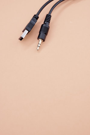 A vertical shot of a wire with a USB end and audio cable on an orange background