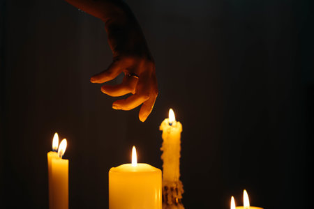 A closeup shot of a hand over burning candles in a dark roomの写真素材