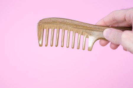 A closeup shot of a hand holding a wooden comb on a pink backgroundの写真素材