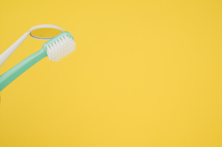 A new green toothbrush and a yellow dental mirror on a yellow backgroundの写真素材