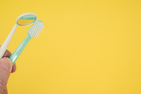 A new green toothbrush and a yellow dental mirror on a yellow backgroundの写真素材