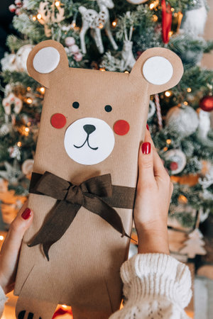 A person holding a beautifully wrapped gift decorated as a bear with a black ribbon near the Xmas...
