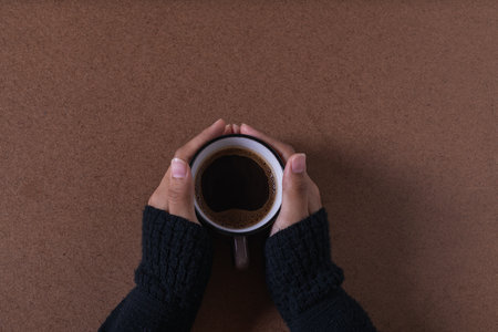 A top view of female hands holding a coffee mug on a brown surfaceの写真素材