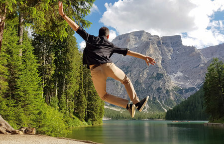 A shallow focus of a person jumping and heel kicking near a lake surrounded by rocky hillsの写真素材