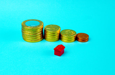 A high angle shot of coins stacked with a miniature house on blue background