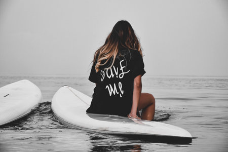 A young long hair female sitting on a surfboard and enjoying the scenery of the calm seaの写真素材