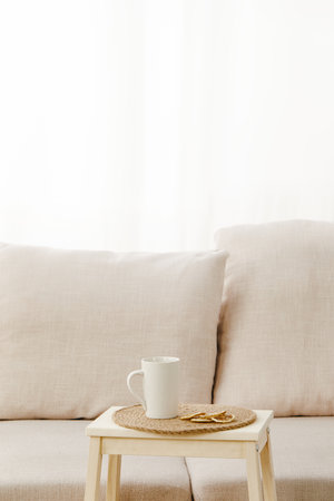 A vertical shot of a small table with a mug on it near a beige sofa under the lightsの写真素材