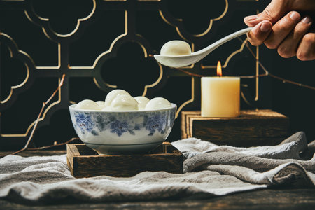 A closeup of a person taking a glutinous rice ball with a spoon from a bowl on the table