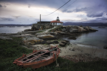 A beautiful shot of a boat near the shore with the Punta Cabalo lighthouse in Galicia, Spainの写真素材