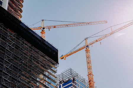 A low angle of two cranes in a construction site under a clear sky backgroum