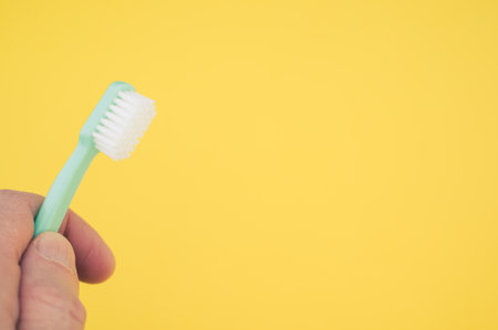 A closeup of a hand holding a toothbrush isolated on yellow background with an empty space for a textの写真素材