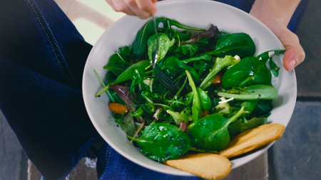 A closeup of female hands holding a bowl of fresh spinach salad and a forkの写真素材