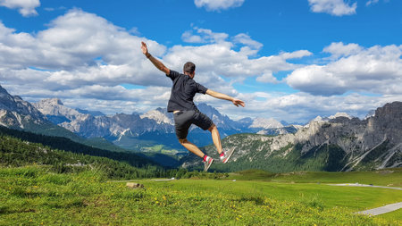 A hiker jumping up on the grass-covered meadow overlooking the beautiful mountains