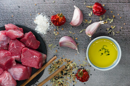 A top view of raw cut meat, garlic cloves, dried pepper, oil on the table - making dinner