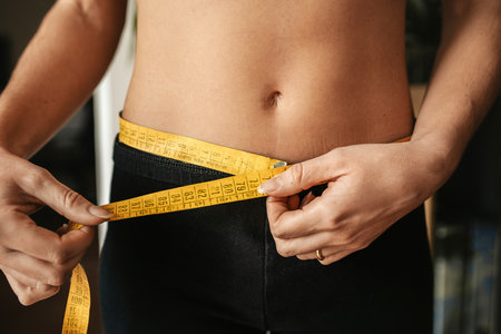 A closeup of a young female measuring her waist with a measuring tape - the concept of weight loss,...