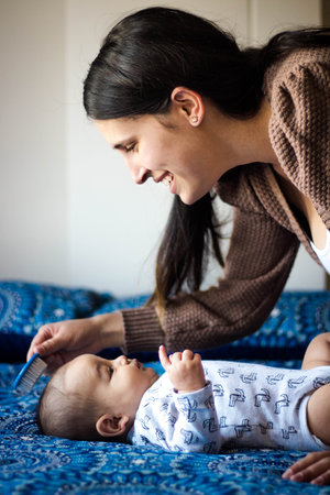 A shallow focus of a young happy mother brushing her child's hair lying on a bed