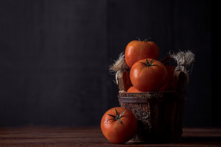 A closeup view of tomatoes with waterdrops on it placed in a wooden bowl on a wooden tableの写真素材