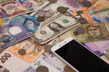 A high angle shot of a smartphone on different cash bills and coins on the table