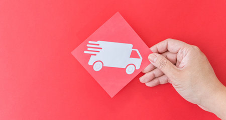 A female hand holding delivery truck shape symbol on red backgroundの写真素材