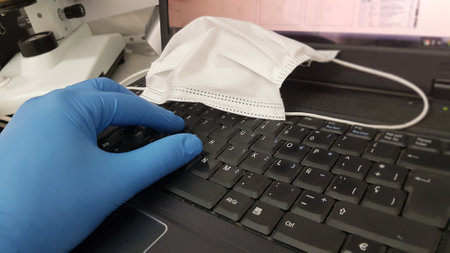 A closeup shot of a researcher or scientist's doing research on the computer with a medical face mask on the keyboardの写真素材