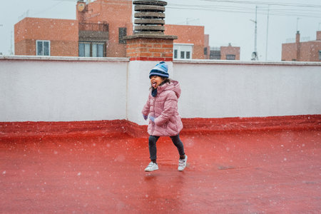 A portrait of a funny cute girl in a warm winter coat and hat catching snowflakes on her tongueの写真素材