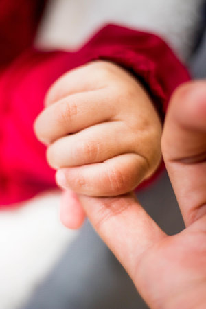 A vertical shot of a newborn child holding an adult female's finger with a blurry backgroundの写真素材