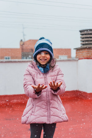 A closeup portrait of a cute lovely girl playing with fresh snow during a snowfall in the wintertime