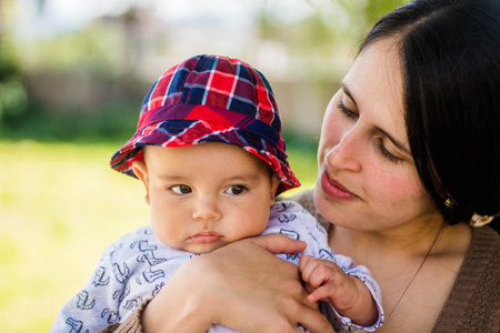 A shallow focus of a young mother hugging her newborn child with a bucket hat in a park on a sunny