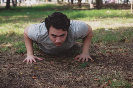 A shallow focus of a young male doing push-ups in a park under the sunlightの写真素材