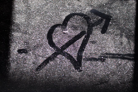 A closeup of a drawing of a heart and an arrow on a frozen window