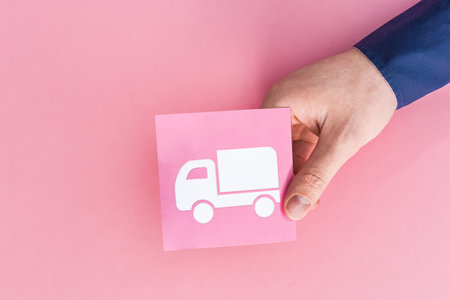 A closeup of a person holding a delivery truck sign isolated on a pink backgroundの写真素材