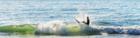 A panoramic shot of a surfer on the board in a wavy seaの写真素材