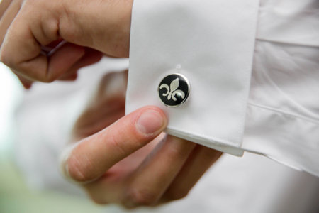 A closeup shot of a groom's hand fixing the cufflinks of his white shirt before the wedding ceremony