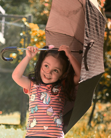 A cute smiling Caucasian little girl holding an umbrella on a sunny day
