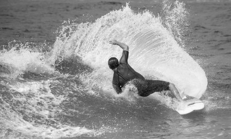 A grayscale shot of a surfer on the board in a wavy sea