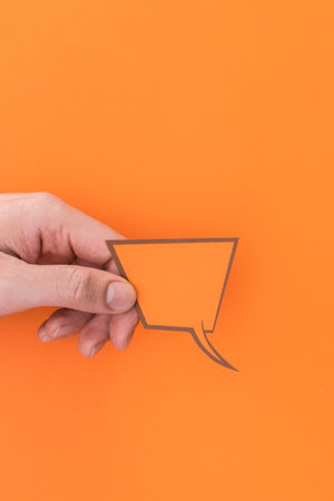 A vertical shot of a person holding a speech bubble icon isolated on an orange backgroundの写真素材
