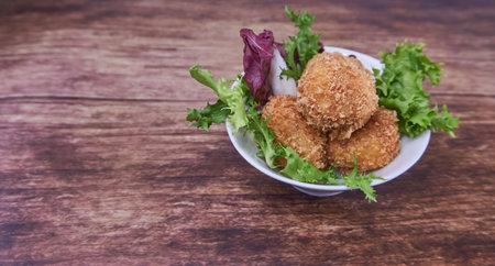 A ration of homemade ham croquettes on a white plate on rustic wooden backgroundの写真素材