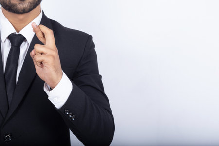 A midsection of a businessman wearing a black suit holding his fingers crossed against a white backgrouの写真素材