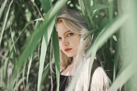 A portrait of a sensual female with blonde hair looking behind the green leavesの写真素材