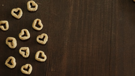 A top view of heart-shaped cereal pieces scattered on the left side of a wooden surface with a copy spaceの写真素材