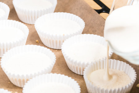 A closeup of cheesecake batter pouring into cupcake liners on a sheet pan