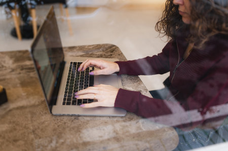 A shallow focus of a curly young woman working in front of her laptop in a cafe