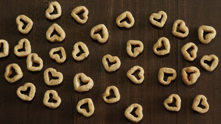 A top view of heart-shaped cereals scattered in a chaotic order on the wooden