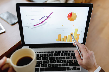 An overhead shot of a man holding a pen and a cup of dark coffee pointing at the desktop while analyzing final dataの写真素材
