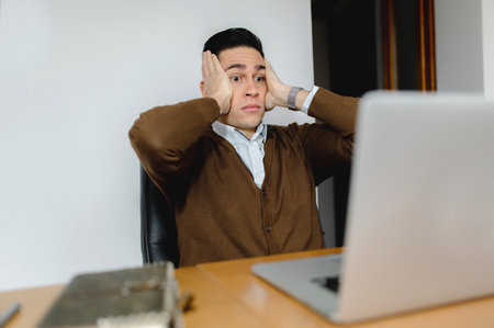 A portrait of an anxious young employee working on his laptop in the office
