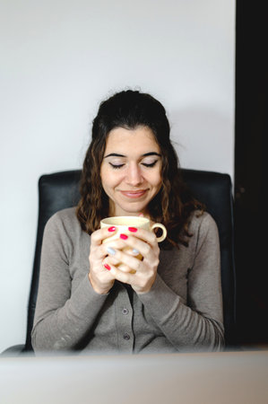 A vertical shot of a woman holding a mug in front of a laptopの写真素材