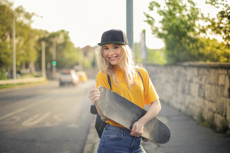 An attractive Caucasian female holding a skateboard while standing by the streetの写真素材