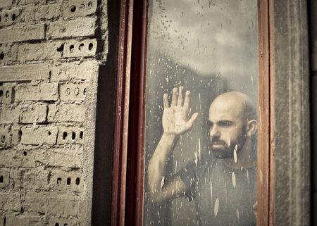 An adult lonely depressed man looking out of the window on a gloomy day