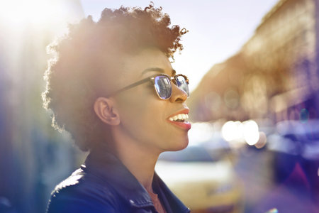 A shallow focus of a smiling African woman with sunglasses and short curly hair under the sunlight
